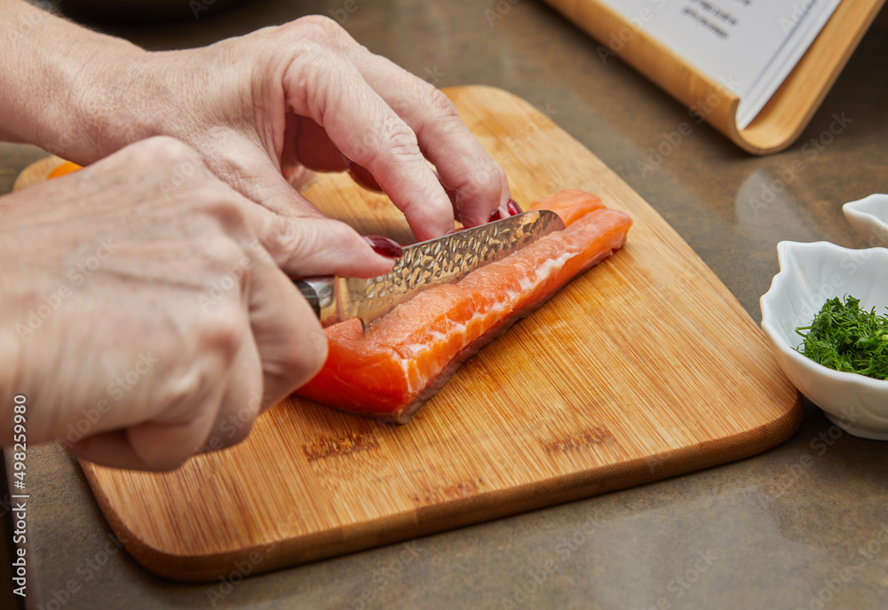 Wall mural Chef cuts salmon with knife to prepare recipe