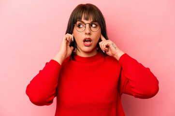 Young caucasian woman isolated on pink background covering ears with fingers, stressed and desperate by a loudly ambient.