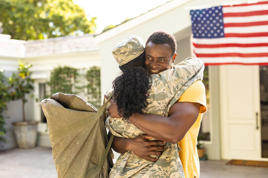 Female mid adult african american soldier embracing smiling husband on arrival at home