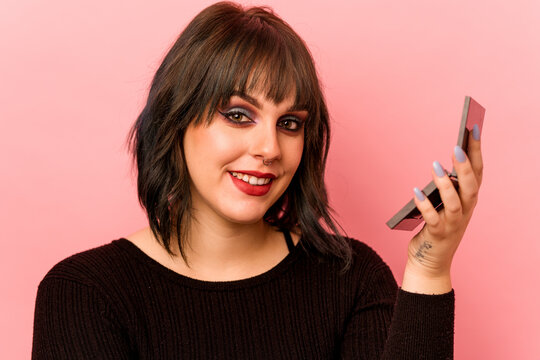 Young caucasian woman holding eye shadows isolated on pink background