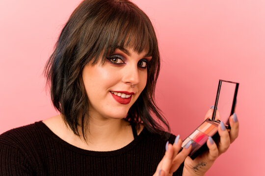 Young caucasian woman holding eye shadows isolated on pink background