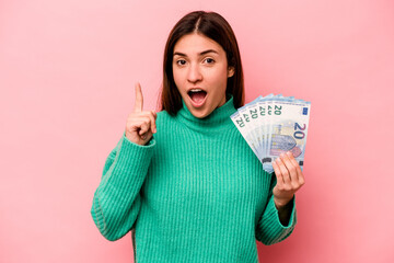 Young caucasian woman holding banknotes isolated on pink background having an idea, inspiration concept.
