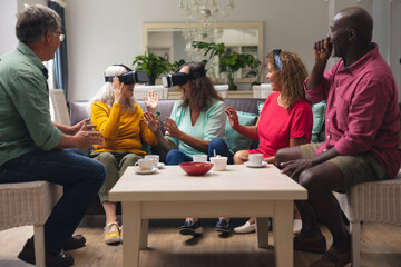Happy multiracial senior woman and men with friends using vr headsets in living room at home
