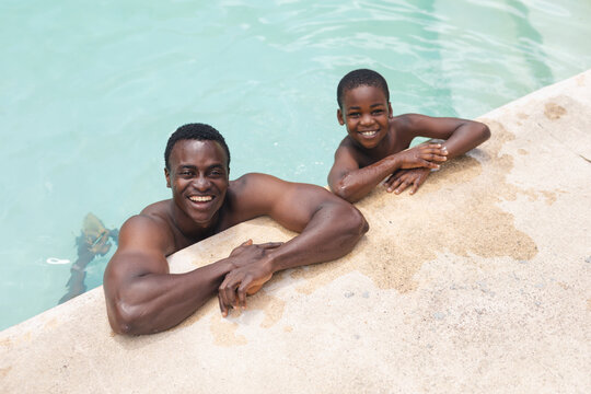 High Angle Portrait Of African American Happy Shirtless Father And Son In Swimming Pool