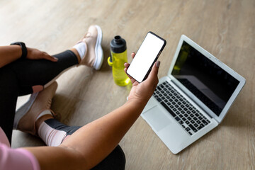 Low section of african american mid adult woman using smart phone and laptop while exercising - Powered by Adobe