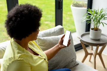 African american mid adult woman using smart phone with blank screen while sitting on sofa at home