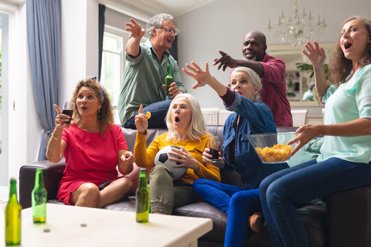 Shocked multiracial senior friends watching soccer match on tv at home