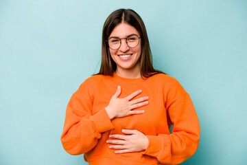 Young caucasian woman isolated on blue background laughs happily and has fun keeping hands on...