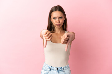 Young woman over isolated pink background showing thumb down with two hands