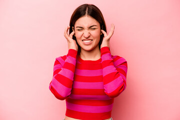 Fototapeta premium Young caucasian woman isolated on pink background covering ears with hands.