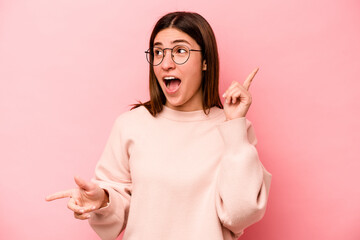 Obraz premium Young caucasian woman isolated on pink background pointing to different copy spaces, choosing one of them, showing with finger.
