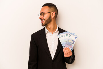 Young business hispanic man holding banknotes isolated on white background looks aside smiling, cheerful and pleasant.