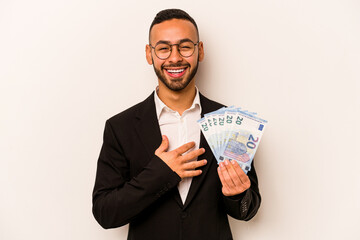 Young business hispanic man holding banknotes isolated on white background laughs out loudly keeping hand on chest.