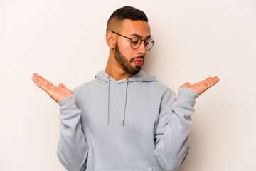 Young hispanic man isolated on white background confused and doubtful shrugging shoulders to hold a...