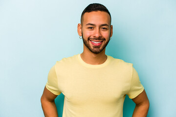 Young hispanic man isolated on blue background confident keeping hands on hips.