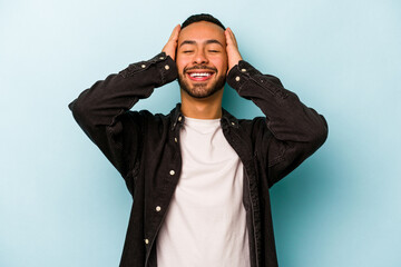 Young hispanic man isolated on blue background laughs joyfully keeping hands on head. Happiness concept.