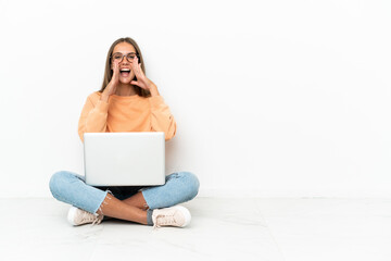 Young woman with a laptop sitting on the floor shouting and announcing something