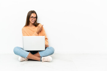 Young woman with a laptop sitting on the floor pointing back