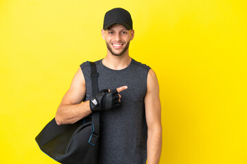 Young sport blonde man with sport bag isolated on yellow background pointing to the side to present...
