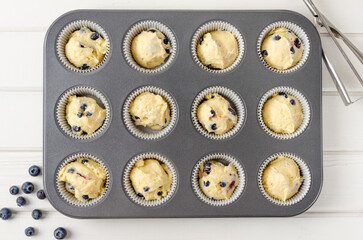 Raw dough for lemon muffins with blueberries and shtreisel in baking form on a white wooden background. Recipe step by step. Top view.