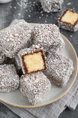 Traditional Australian Lamington cake in chocolate glaze and coconut flakes on a plate on a gray concrete background with a cup of tea. Selective focus.