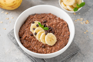 Chocolate oatmeal porridge with banana and chocolate chips on top in a white bowl. Healthy breakfast. Copy space.