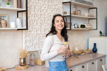 Healthy hydration concept. Happy lady drinking fresh water with lemon for refreshment, standing in...