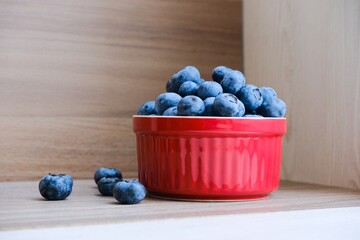 Isolated fresh raw organic blueberries in a red plate on the wooden light table. Healthy nutrition. Minimalistic simple natural neutral template. Superfood. Organic eco health care. Vitamin nutrition.