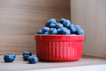 Isolated fresh raw organic blueberries in a red plate on the wooden light table. Healthy nutrition. Minimalistic simple natural neutral template. Superfood. Organic eco health care. Vitamin nutrition.