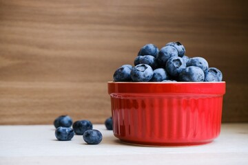 Isolated fresh raw organic blueberries in a red plate on the wooden light table. Healthy nutrition. Minimalistic simple natural neutral template. Superfood. Organic eco health care. Vitamin nutrition.