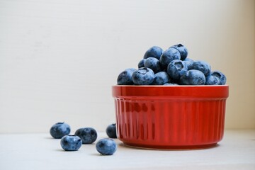 Isolated fresh raw organic blueberries in a red plate on the white light table. Healthy nutrition. Minimalistic simple natural neutral template. Superfood. Organic eco health care. Vitamin nutrition.