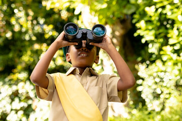 African american scout girl in uniform looking through binoculars while exploring in forest