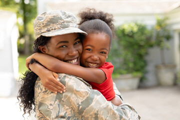 Portrait of happy female mid adult african american soldier embracing daughter outside house