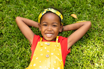 High angle portrait of smiling african american girl lying with hands behind head in backyard
