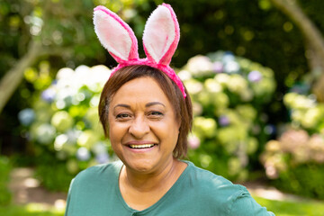 Portrait of smiling african american senior woman wearing pink bunny ears in backyard