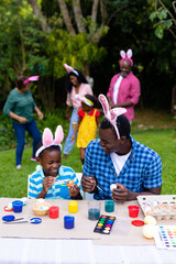 Obraz premium Happy african american boy and father painting easter eggs while family in background