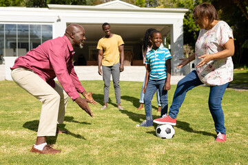 Happy african american multi-generational family playing soccer together in front yard on sunny day