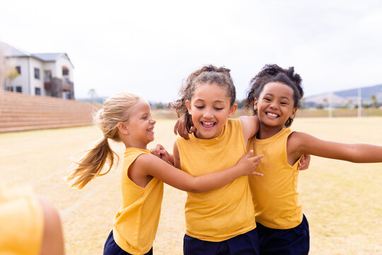 Cheerful multiracial elementary school girls in sports uniform on ground during soccer practice
