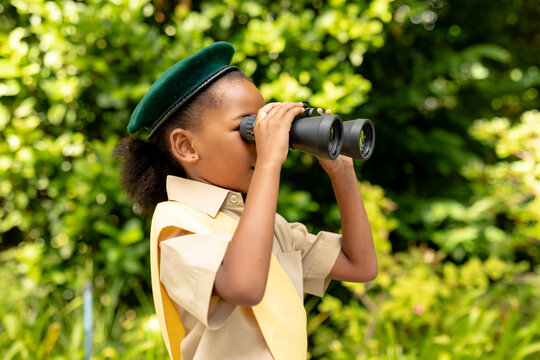 African american scout girl in uniform looking through binoculars in forest