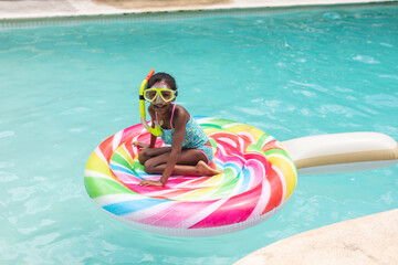 Portrait of happy african american girl with snorkel sitting on inflatable ring in swimming pool