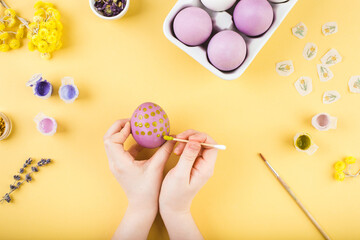 Child hands decorate Easter eggs on yellow background. Happy easter concept.