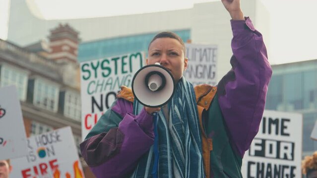 Female protestor using megaphone holding placards and chanting slogans on demonstration march to promote awareness of climate change - shot in slow motion
