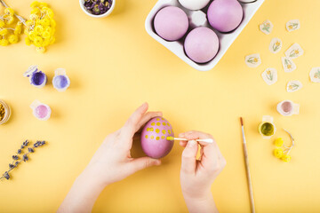 Child hands decorate Easter eggs on yellow background. Happy easter concept.