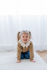 cheerful girl with ponytails crawling on floor at home and looking at camera.