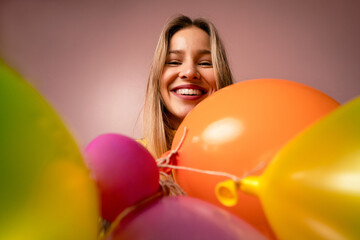 Studio portrait of a happy young blonde woman with balloons over pink background.