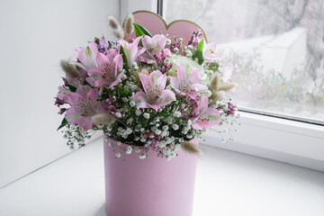 Delicate bouquet of pink lilies, white roses and gypsophila in a love word gift box on the window