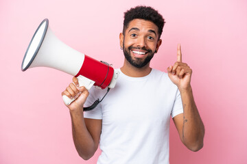 Young Brazilian man isolated on pink background holding a megaphone and pointing up a great idea