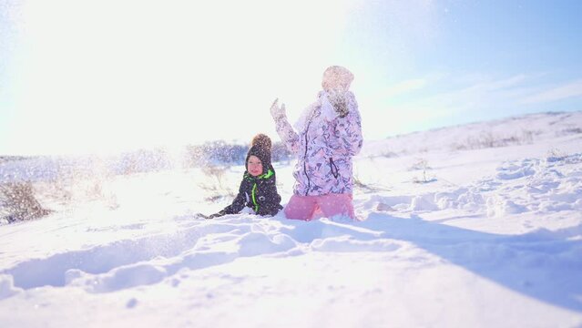 Children playing in the snow. Little boy and old sister outside in the winter park in winter throwing snow. Boy and a girl are walking in the snow in a winter time at sun. Family winter holidays.