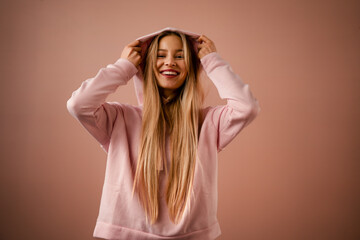 Fashion studio portrait of a happy young blonde woman in hoodie posing over pink background. - Powered by Adobe