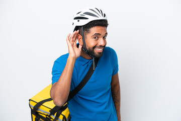 Young Brazilian man with thermal backpack isolated on white background listening to something by putting hand on the ear